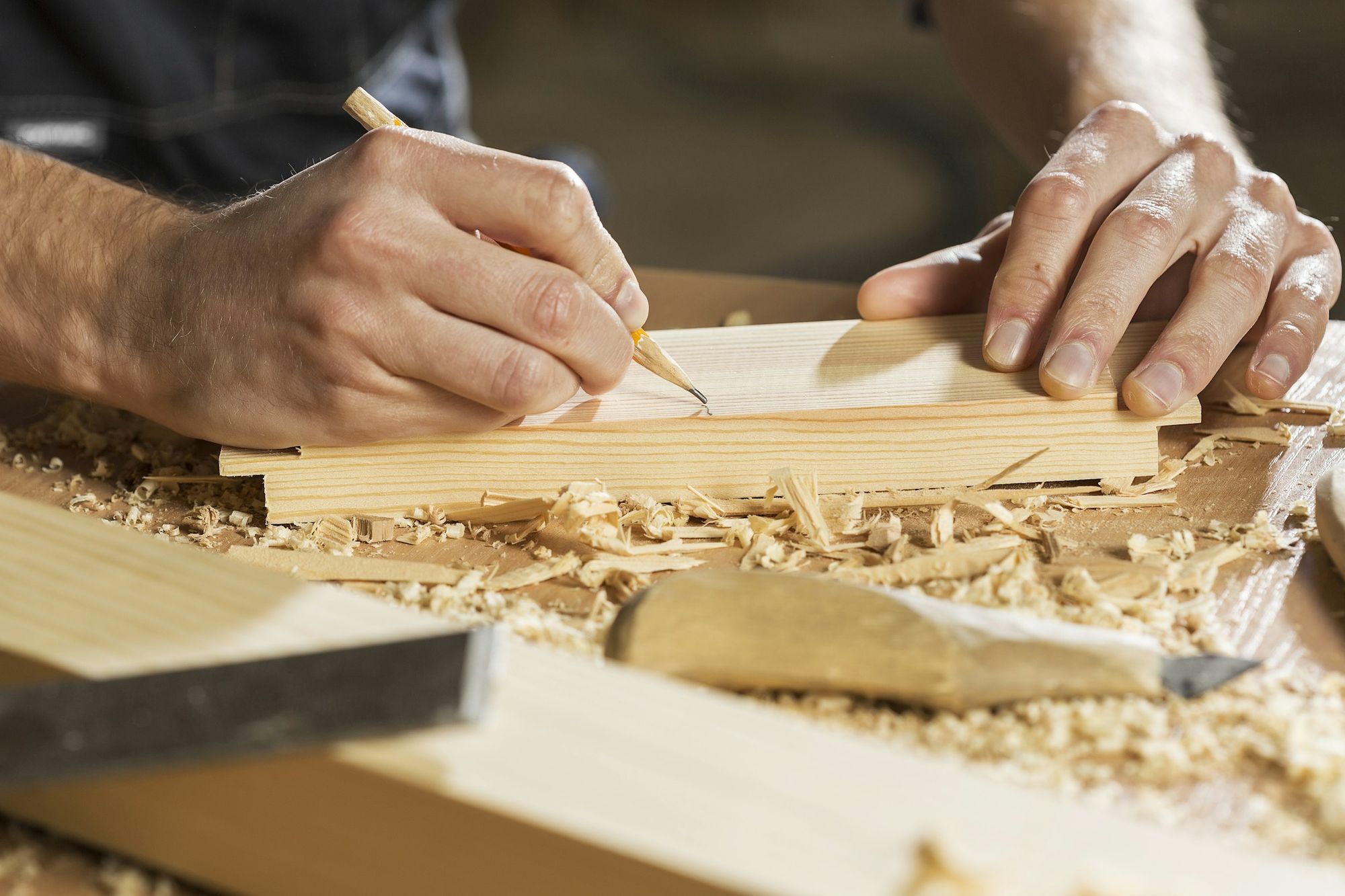 Hände zeichnen eine Linie auf ein Holzbrett, Späne im Licht